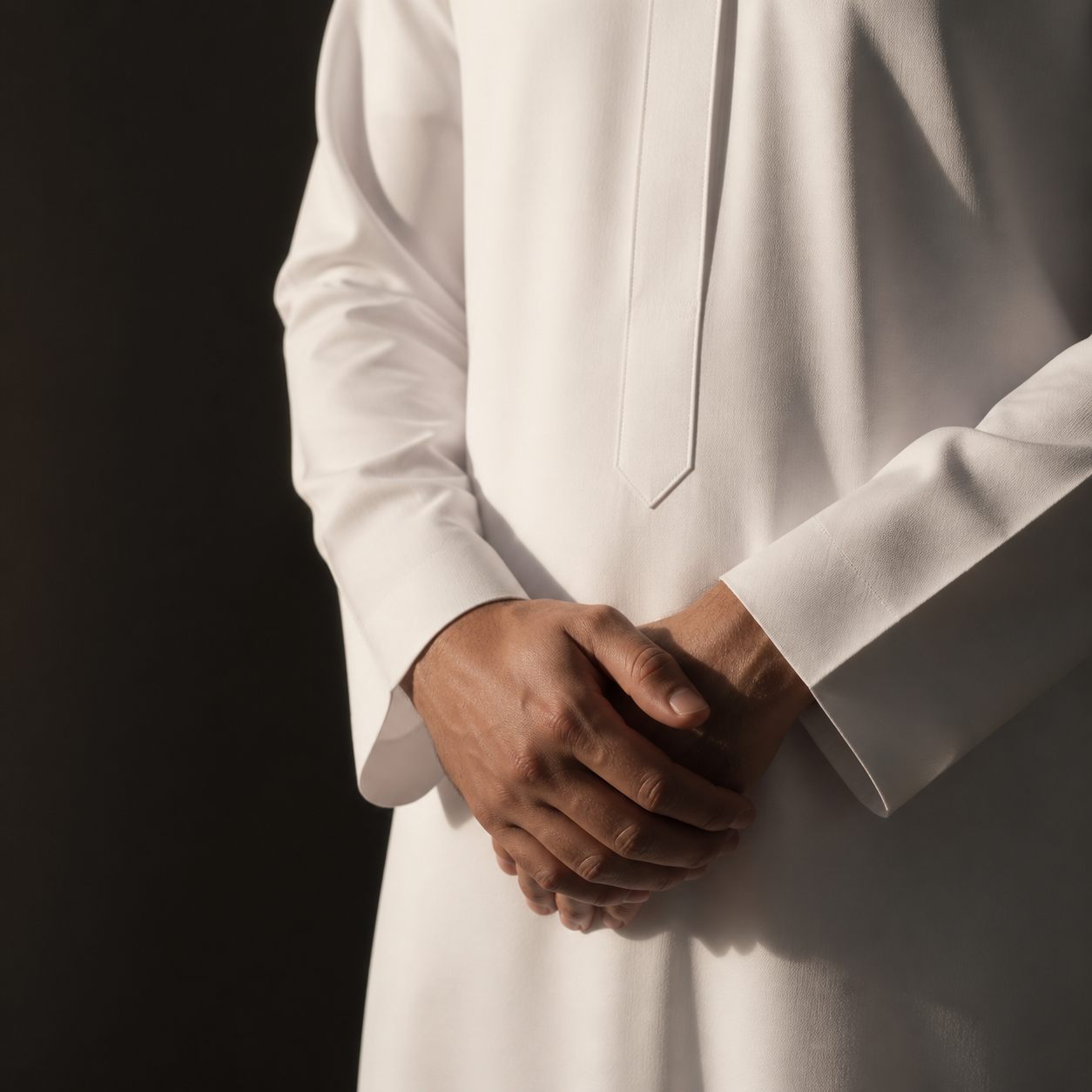 Close-up of a man’s hands folded over a white thobe